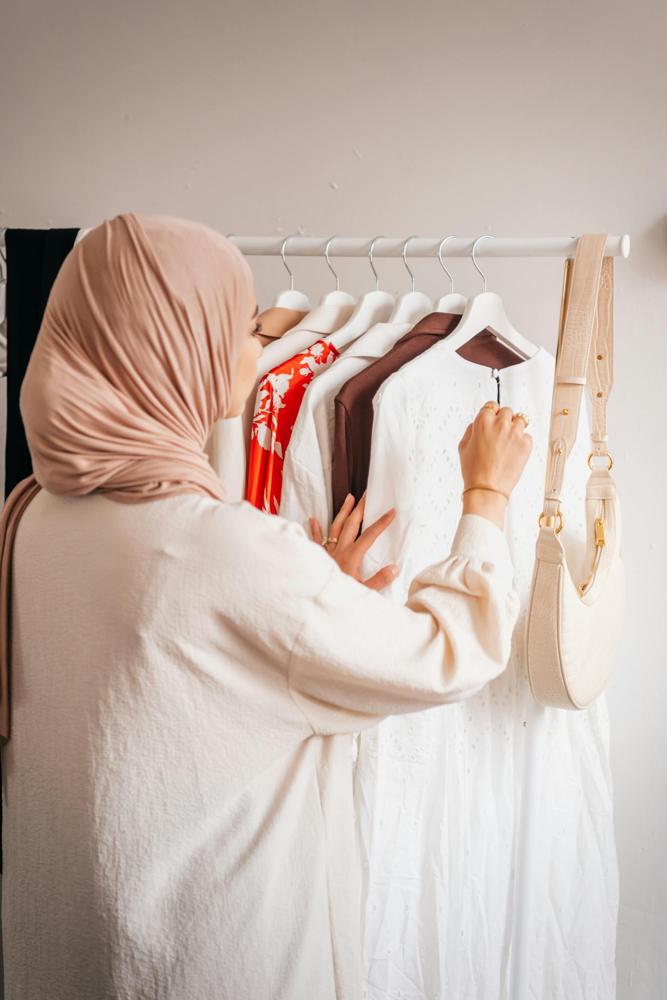 A woman in a hijab selects clothes from a rack, showcasing elegant fashion choices.