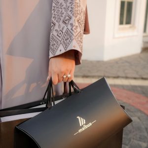 Close-up of a person holding a malbus shopping bag outdoors in stylish attire.