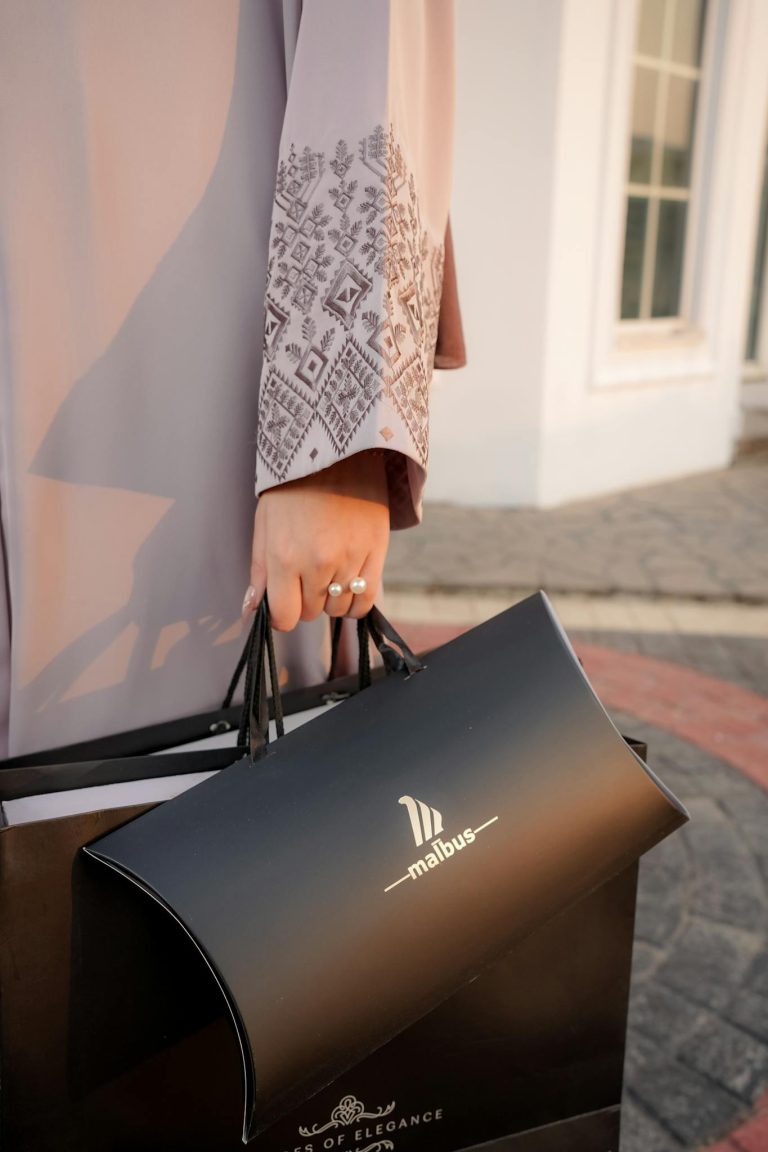 Close-up of a person holding a malbus shopping bag outdoors in stylish attire.