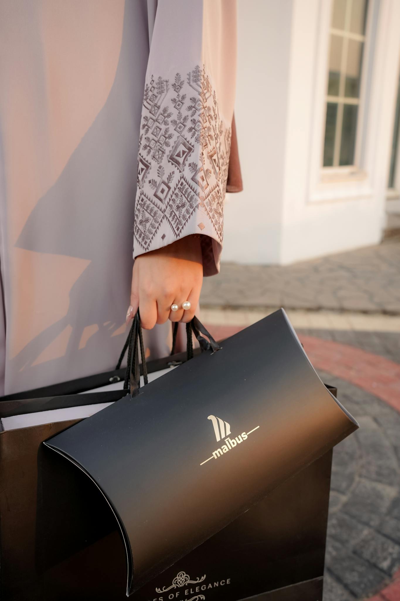Close-up of a person holding a malbus shopping bag outdoors in stylish attire.
