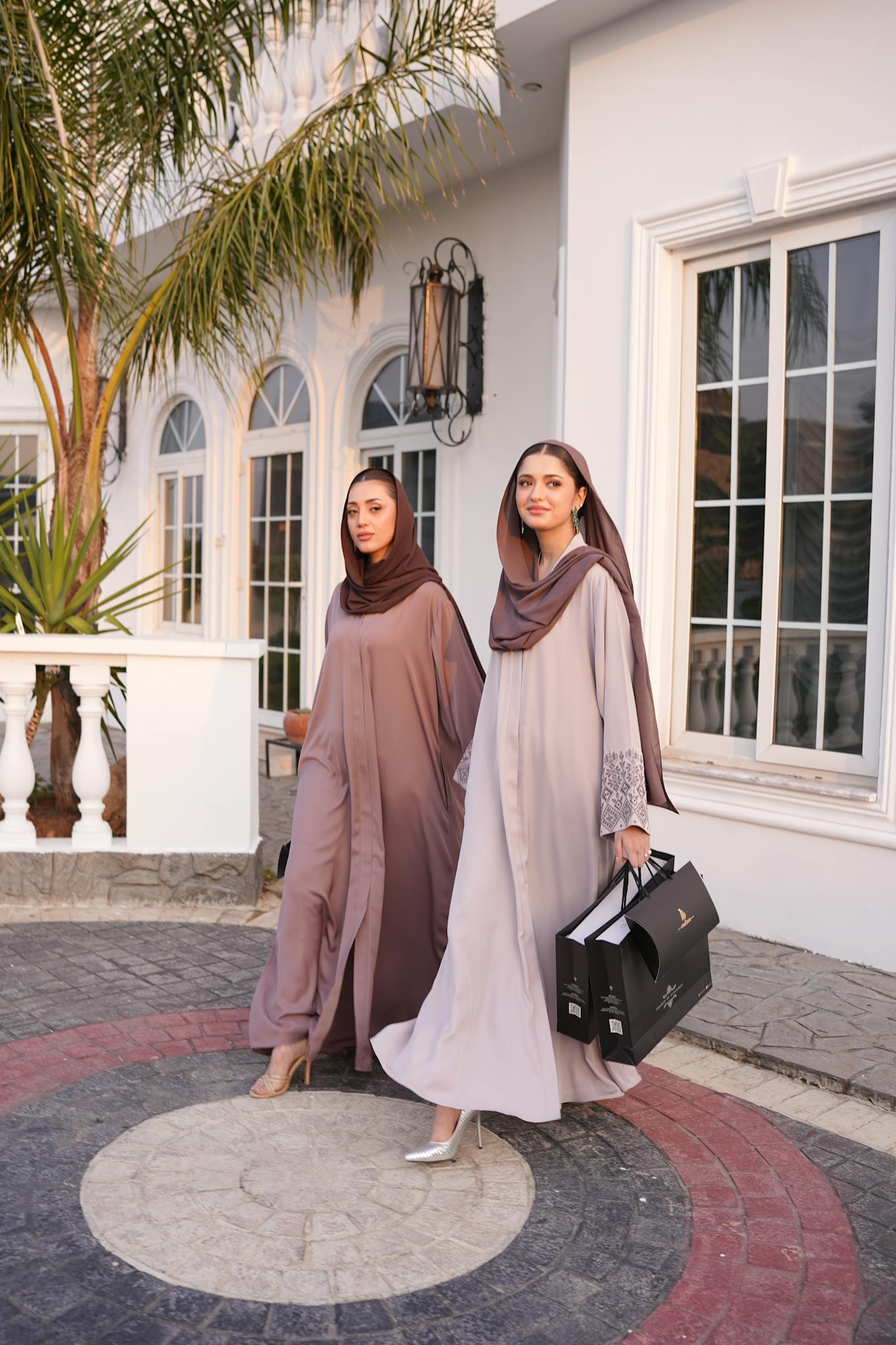 Two women in elegant modest fashion outfits with hijabs walking outdoors.