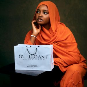 Woman in orange hijab posing with a By Elegant shopping bag, exuding grace and poise.