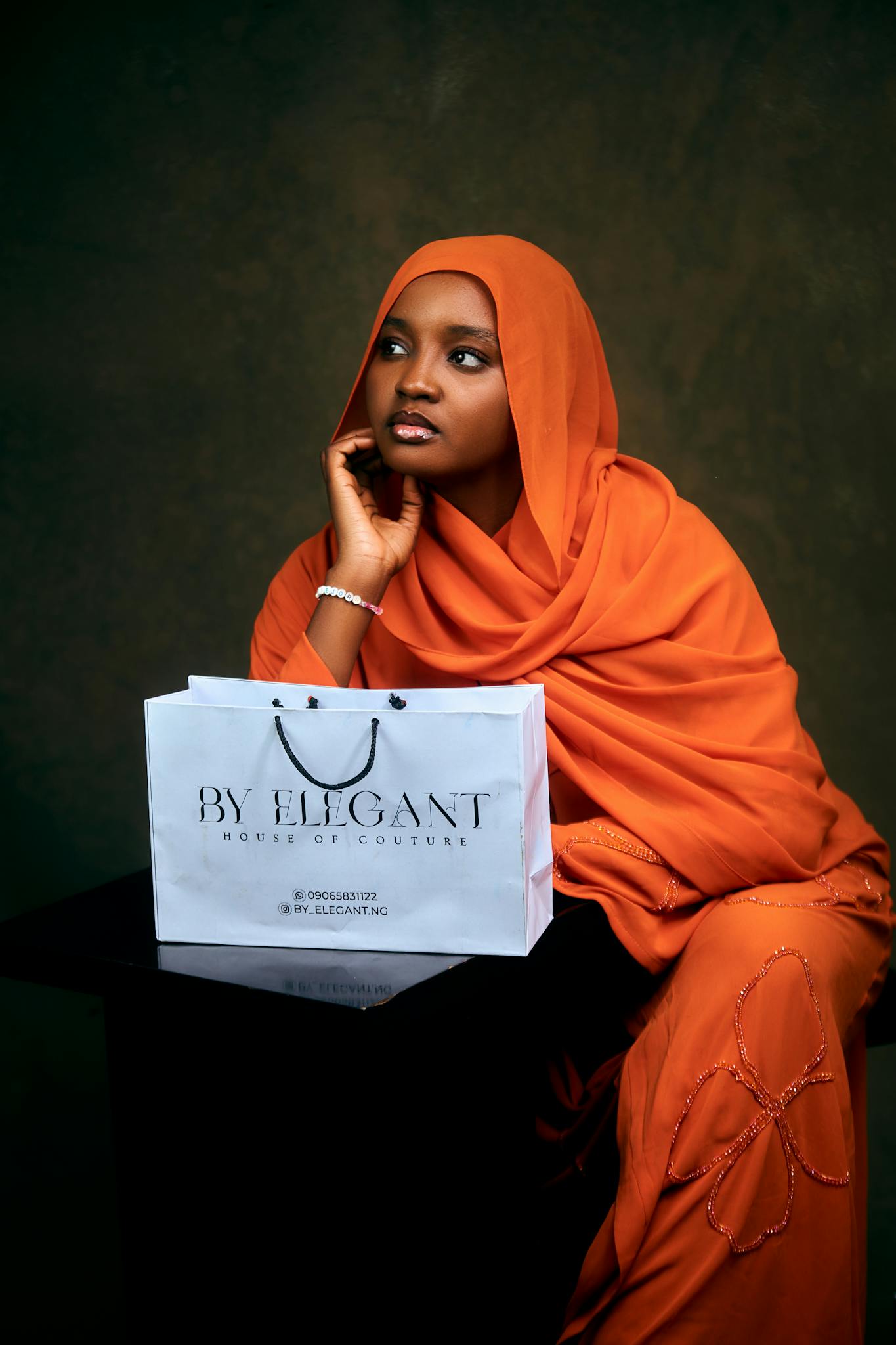 Woman in orange hijab posing with a By Elegant shopping bag, exuding grace and poise.